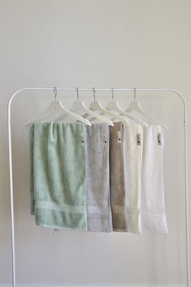 Five pastel bamboo towels displayed on white wooden hangers against neutral background, showing green, gray, brown, cream and