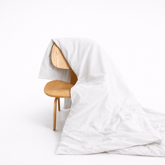 Housse de couette en bambou blanc drapée sur chaise en bois, montrant la texture douce du tissu et la fermeture à boutons cachés