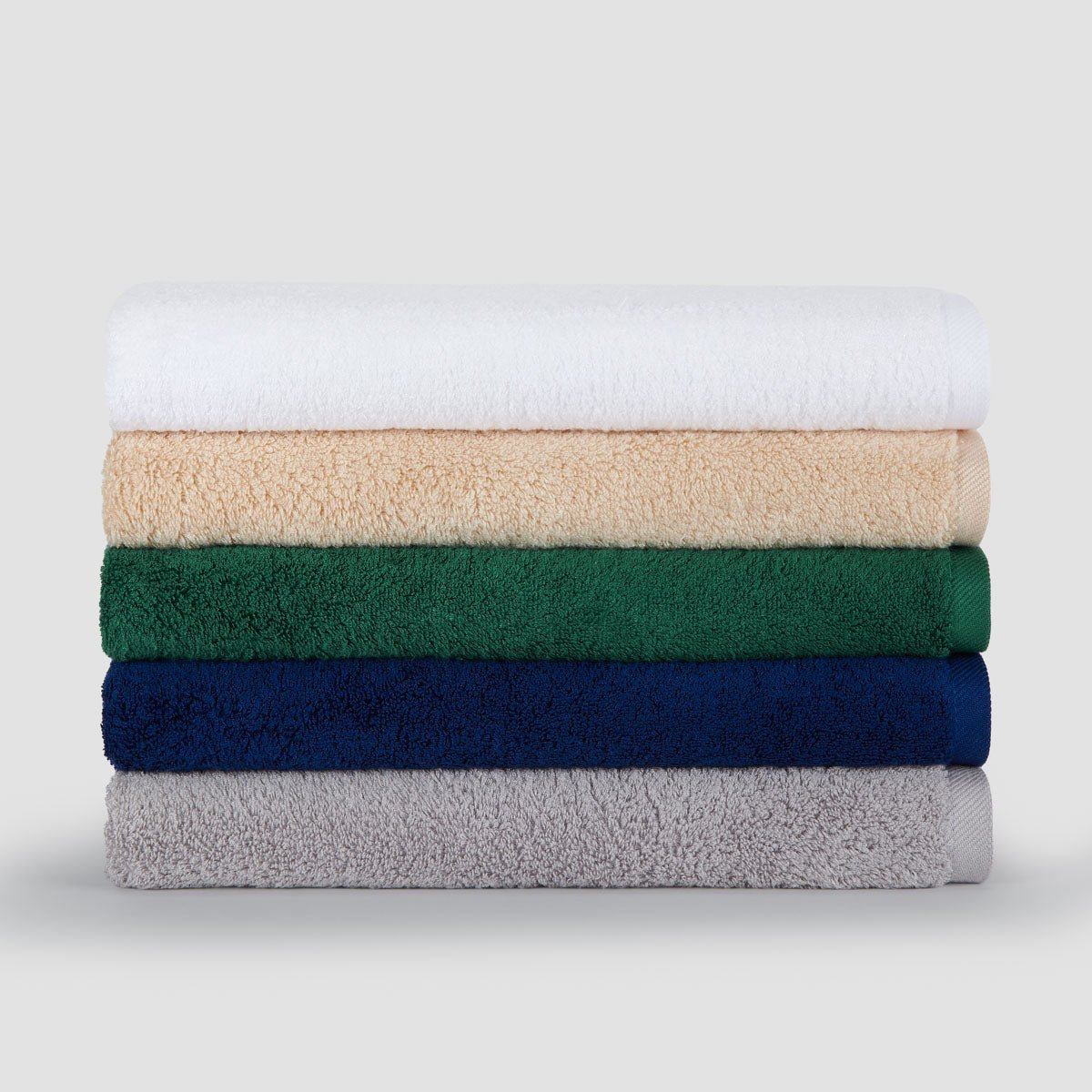 Pile de cinq serviettes en bambou pliées en blanc, beige, vert, bleu marine et gris sur fond clair.
