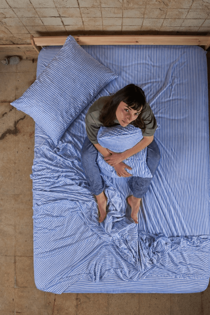 Femme allongée sur le lit portant un ensemble de draps en coton bambou rayé bleu, vue de dessus