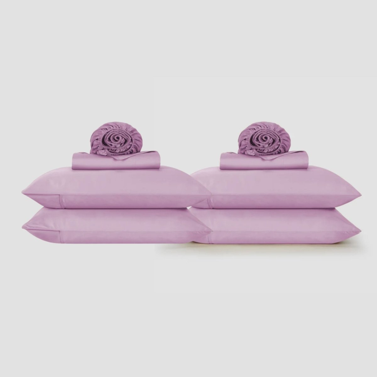 Draps de dessus lavande affichés à plat avec taies d'oreiller assorties et éléments décorés enroulés sur fond neutre