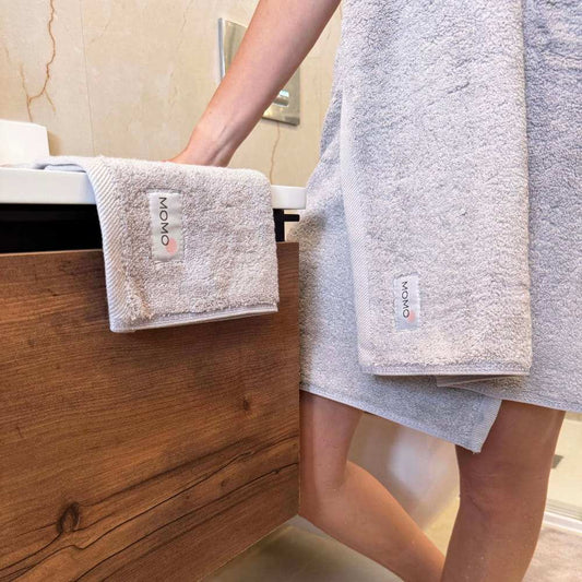 Ensemble de serviettes en coton Momo présenté sur un porte-serviettes en bois avec personne tenant des serviettes beiges pliées