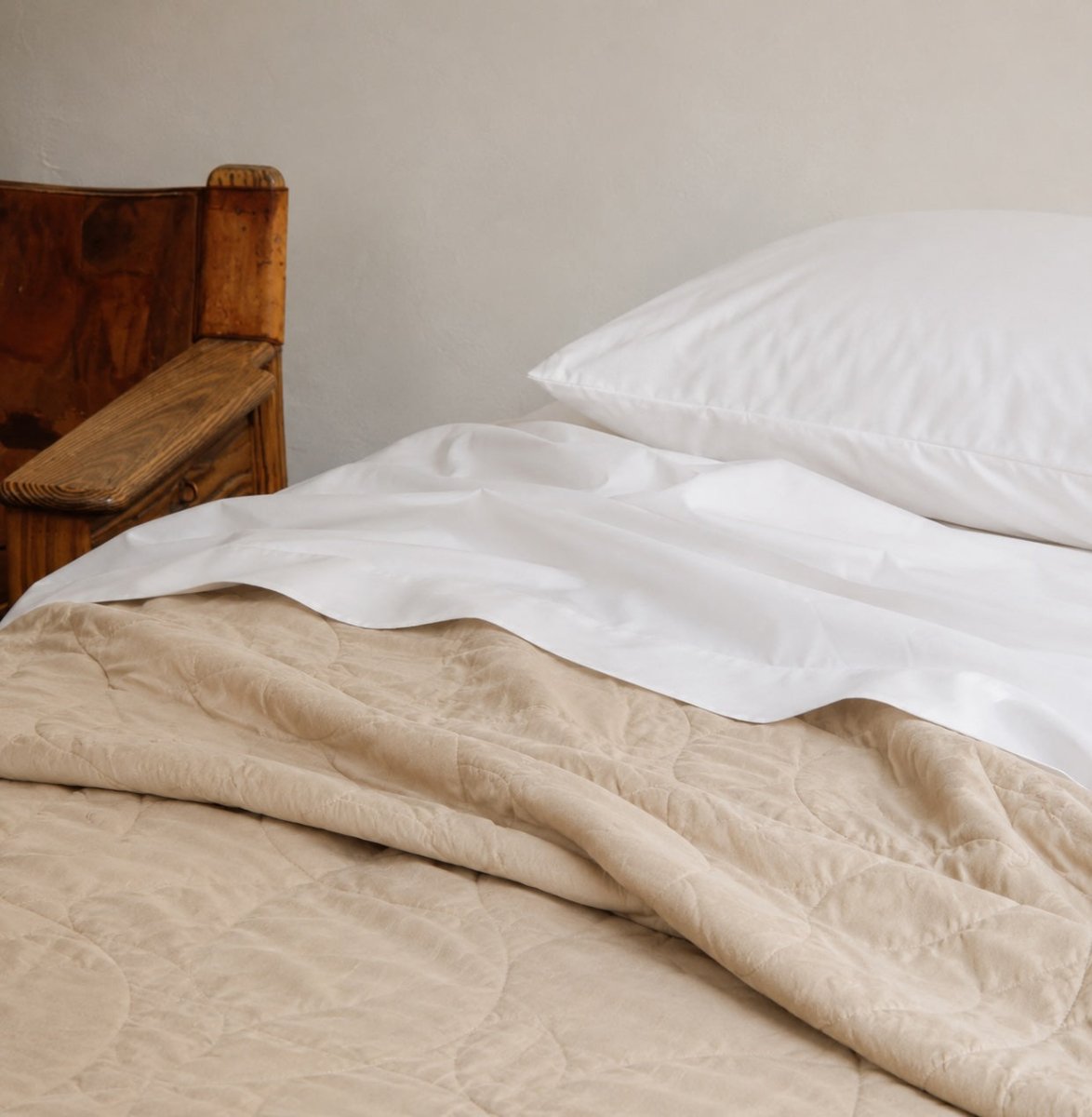 Couvre-lit d'été matelassé beige sur draps blancs avec oreillers sur cadre de lit en bois