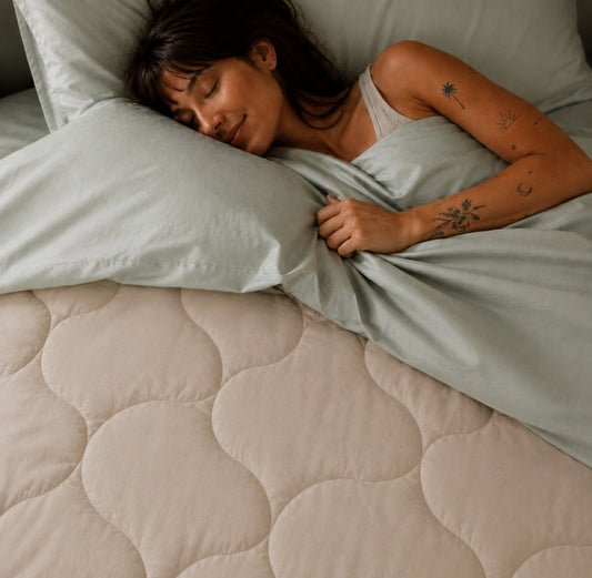 Femme dormant paisiblement sur un lit avec couette matelassée beige et draps gris clair Momo Cotton