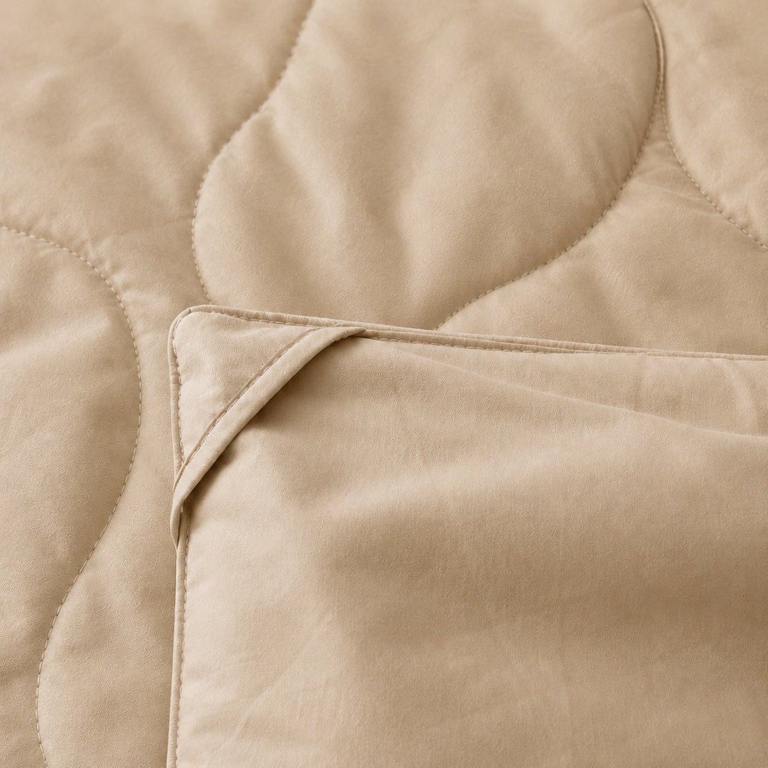 Beige quilted summer bedspread with stitched pattern detail showing soft cotton fabric texture and fold
