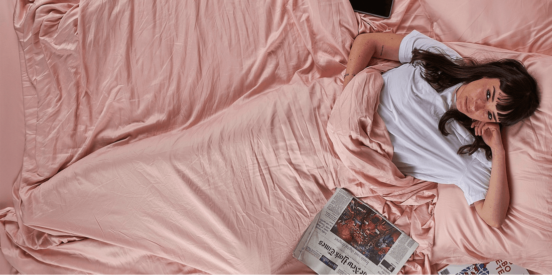 Femme allongée sur un lit avec draps roses lisant un journal, décoration chambre printemps.