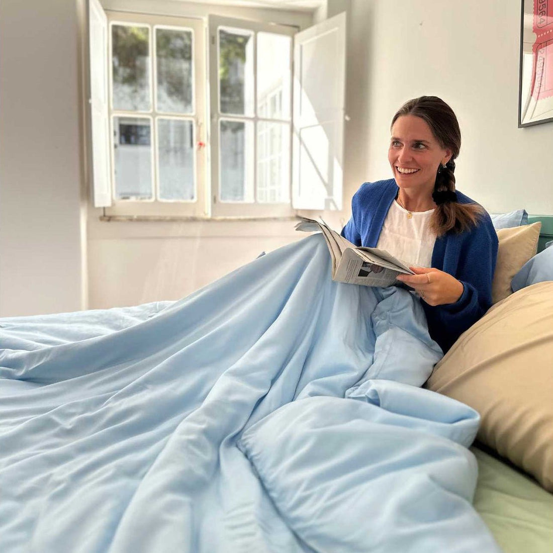 Woman in bed reading newspaper with light blue bedding and pillows
