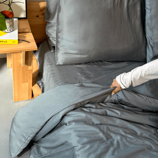 Woman touching grey bamboo bedding on bed with wooden table in background