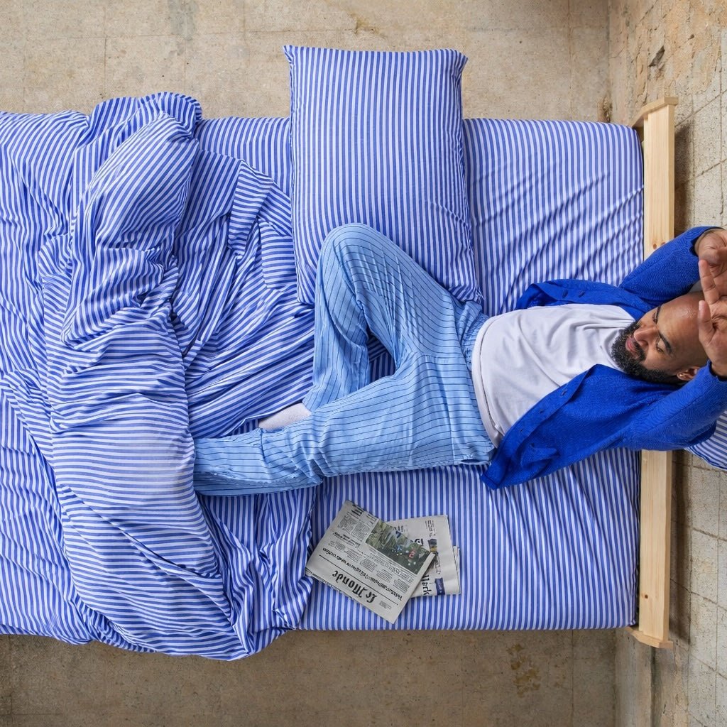 Homme dormant confortablement sur des draps en bambou bleus et blancs rayés.