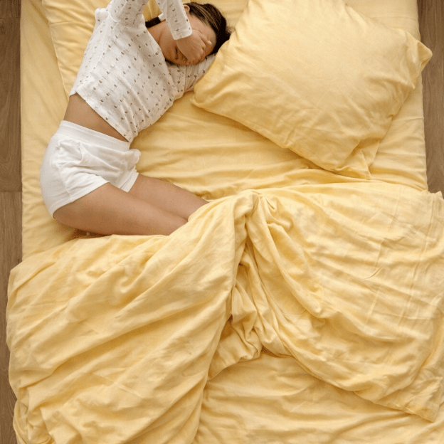 Lit avec parure de lit jaune et oreiller, personne allongée dans une pose de bedscaping décorateur.