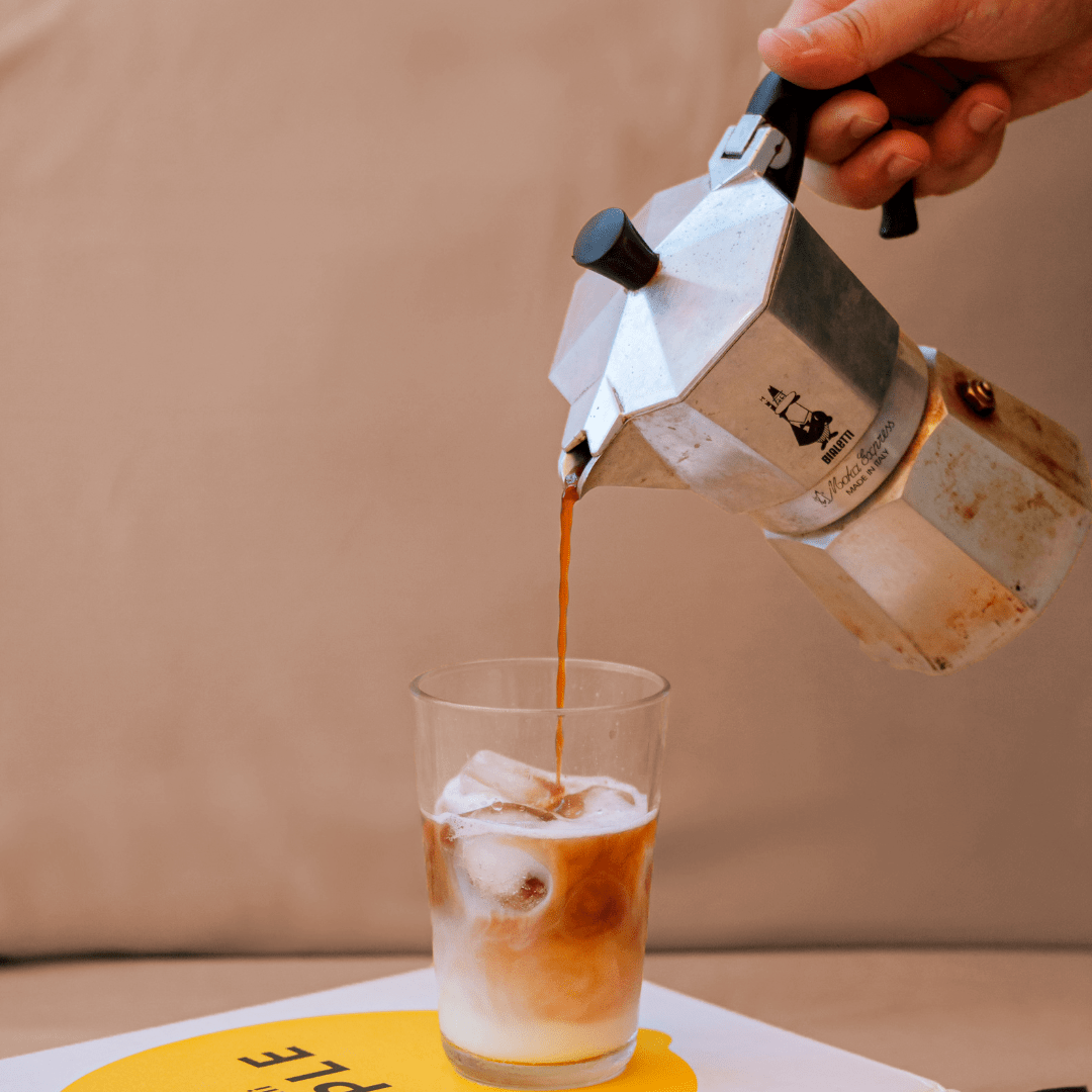 Moka chaud versé dans une tasse avec glaçons sur fond beige.