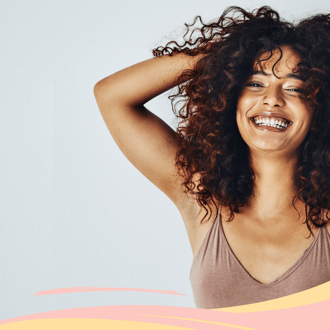 Femme aux cheveux bouclés châtains souriante, affichant des cheveux hydratés et sains.