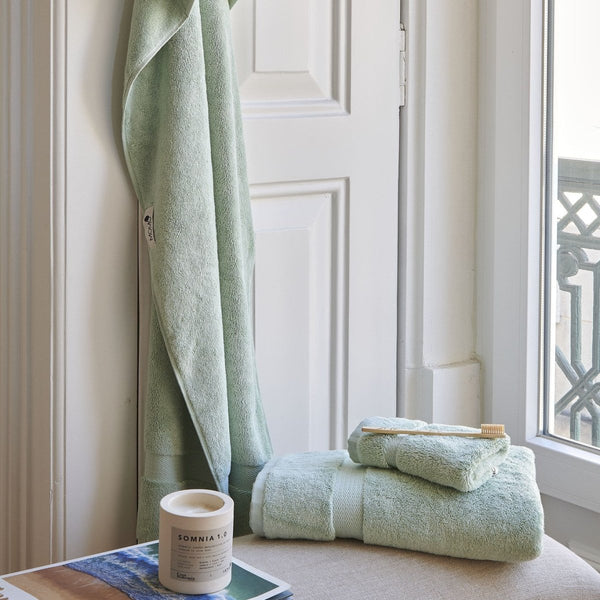 Ensemble de serviettes en bambou vert menthe Alba sur le rebord de fenêtre avec serviettes roulées et brosse à dents