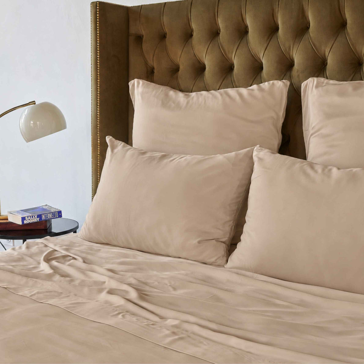 Drap de lit crème sur un lit avec tête de lit capitonnée marron et oreillers beige
