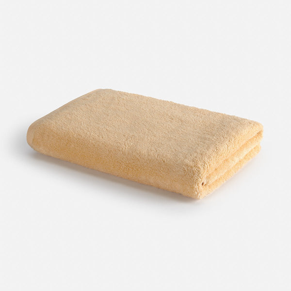 Serviette de bain Wabi-sabi beige pliée sur fond blanc, 70x140cm par Momo Cotton