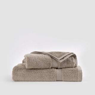Ensemble de serviettes en bambou beige empilées montrant gant de toilette, serviette et drap de bain sur fond blanc