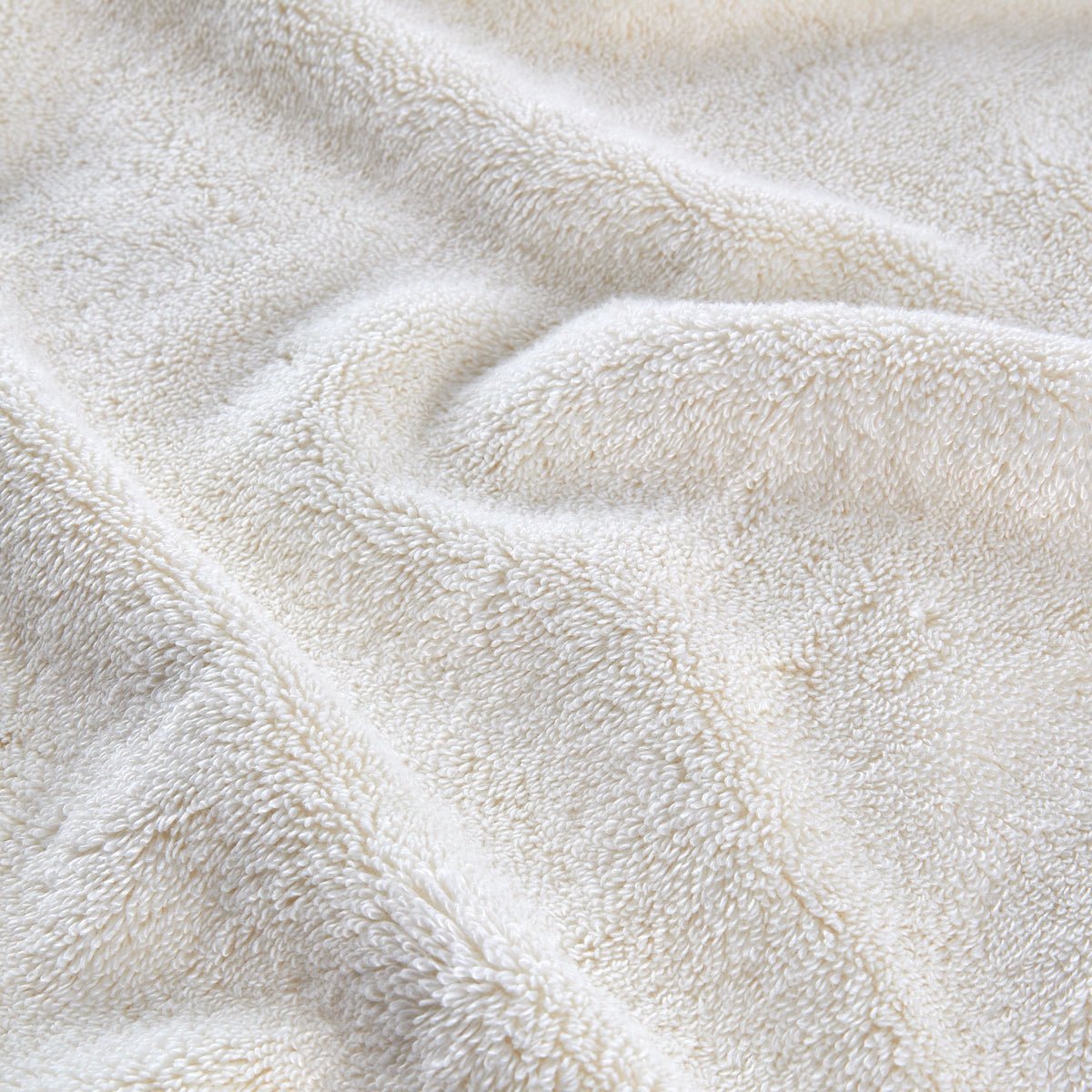 Ensemble de serviettes en bambou couleur crème plié et empilé, montrant texture douce et détails de fibres naturelles