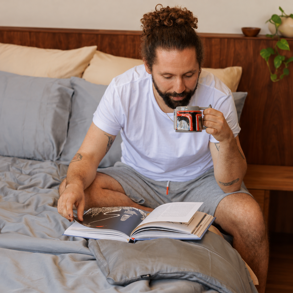 Man in bed with white bedding set reading magazine with cup in hand
