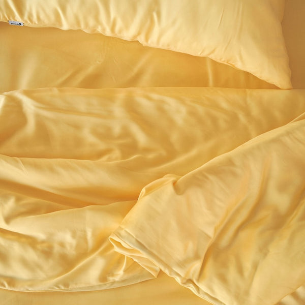 Ensemble de literie en bambou crème avec oreillers et couette repliés, montrant la texture douce et la trame de qualité