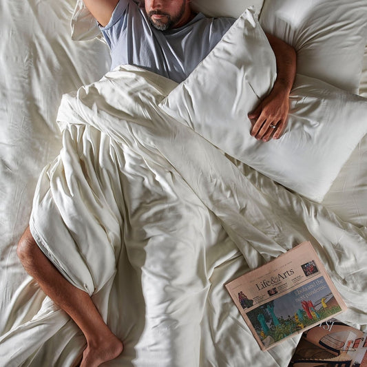 Homem dormindo em jogo de cama de bambu branco com almofada e edredom, vista de cima com jornal