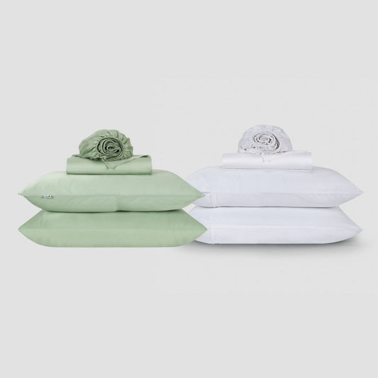 Deux parures de draps Momo en coton côte à côte, une vert sauge et une blanche, empilées avec du linge plié