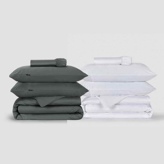 Two Momo Cotton duvet cover sets displayed side by side, one in charcoal gray and one in white, stacked with pillows