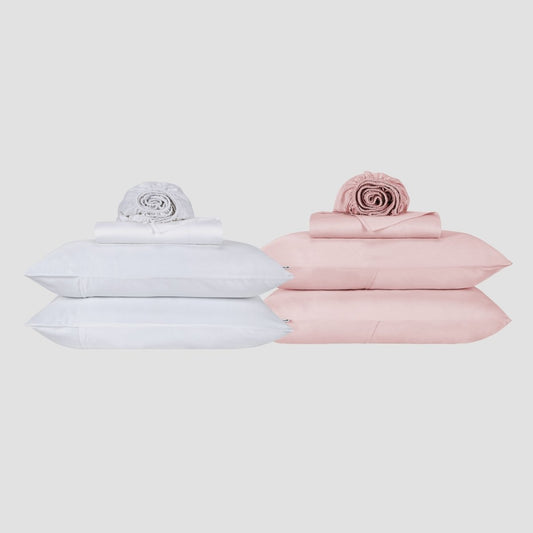Ensemble de draps blanc et rose empilé avec oreillers et couette roulée sur fond neutre