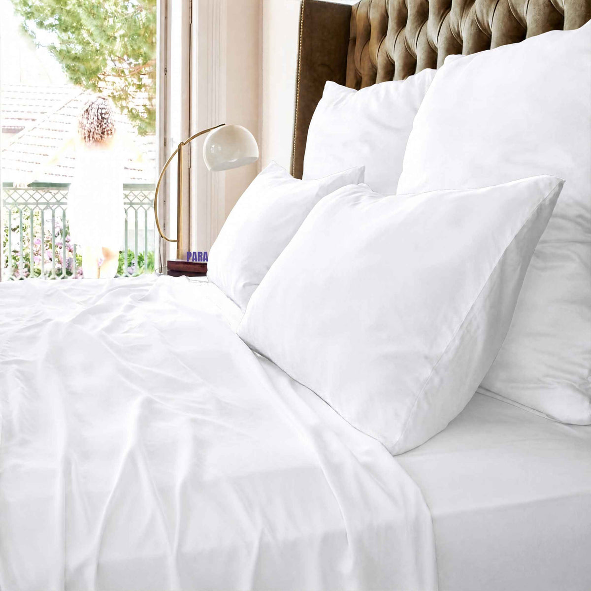 Drap blanc sur lit avec oreillers et tête de lit capitonnée près d'une fenêtre avec vue sur balcon