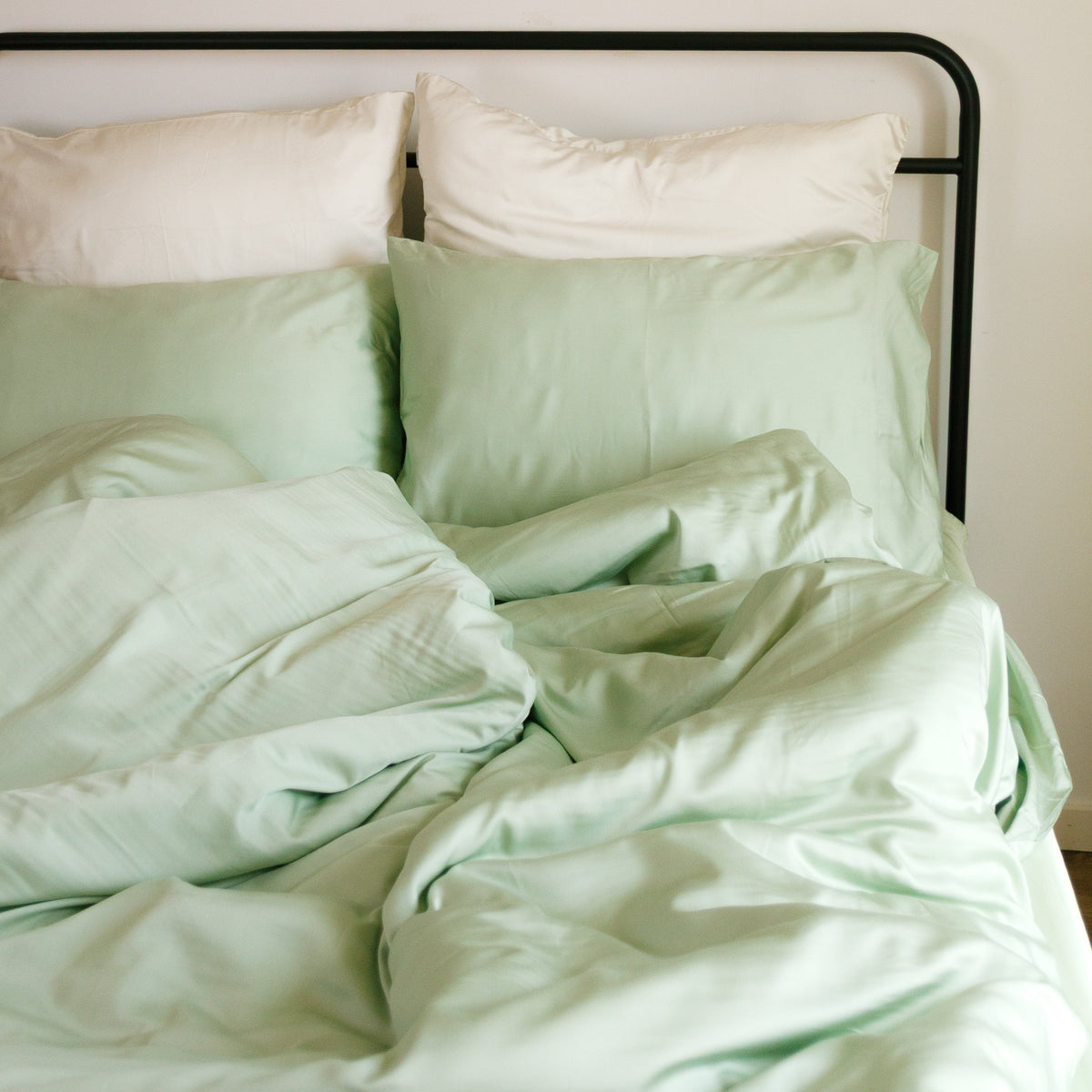 Parure de housse de couette vert clair et blanc sur lit à structure noire, décoration murale avec assiettes en rotin