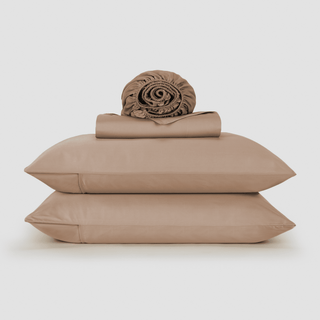 Ensemble de draps en bambou beige empilé avec couette roulée et deux oreillers sur fond blanc