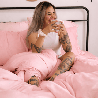 Femme allongée confortablement sur des draps en bambou rose, soulignant la texture soyeuse et le drapé délicat.