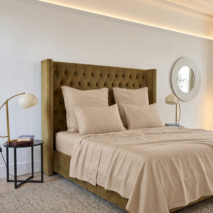 Ensemble de drap housse beige sur lit avec tête de lit rembourrée, oreillers et miroir rond mural